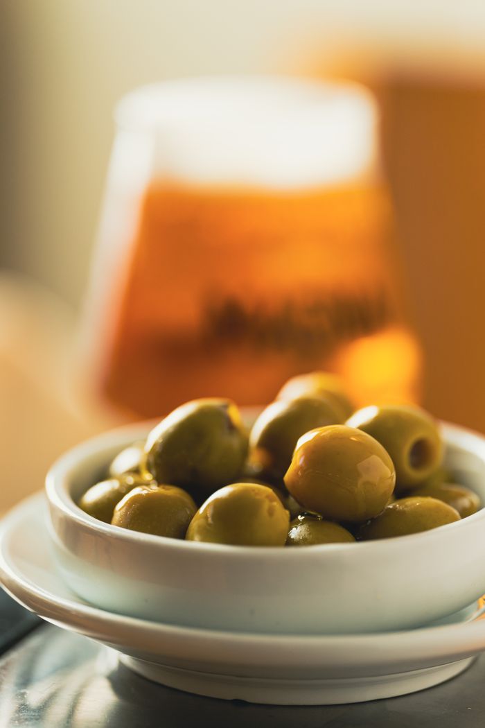 The Art of Drawing Readers In: Your attractive post title goes here Bowl of green olives in focus with a blurred beer glass in the background.